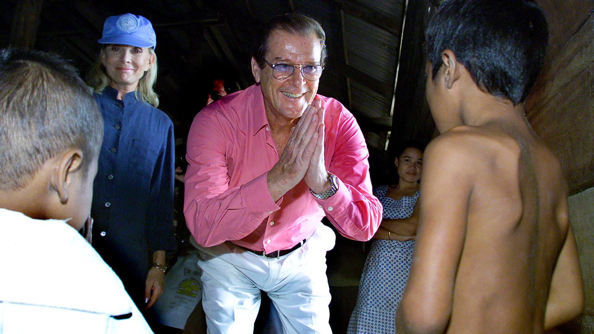 UNICEF Goodwill Ambassador, Roger Moore, and his wife greet a child at a village in Cambodia on Penh on October 23, 2003