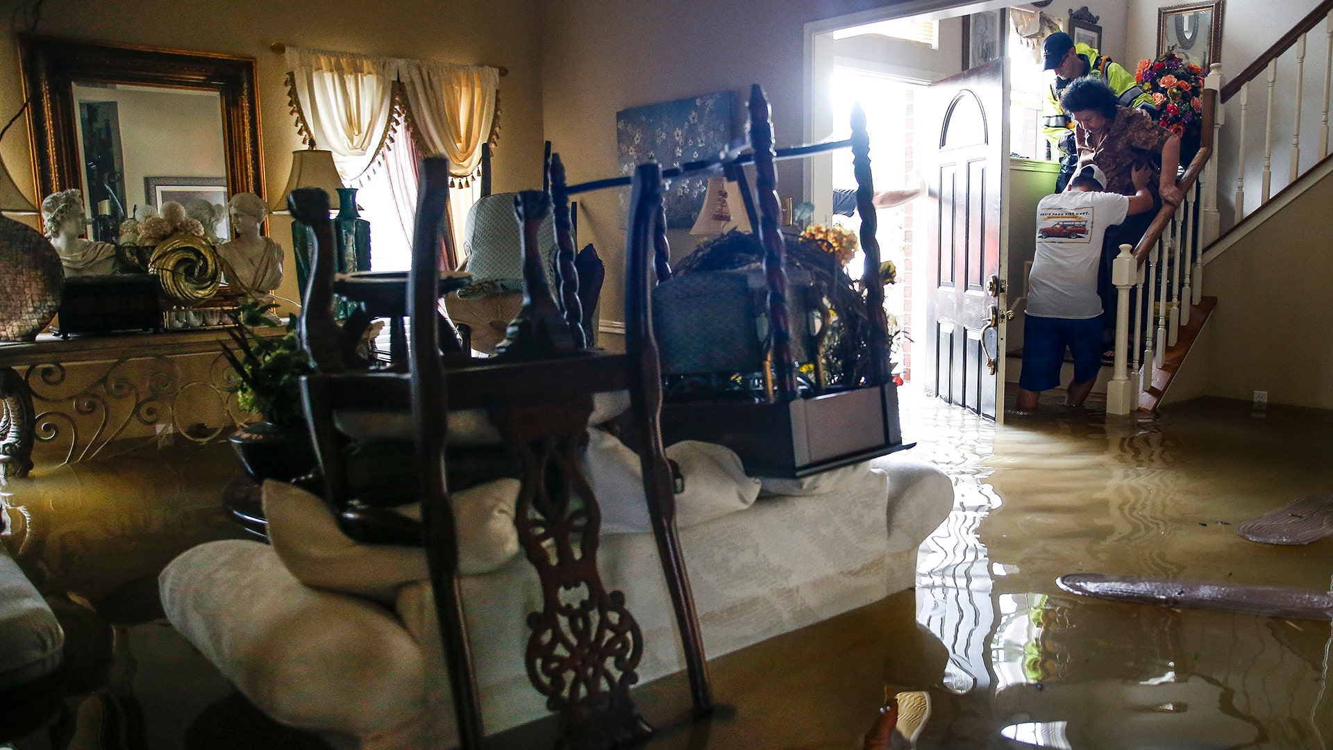 Chris Gutierrez helps his grandmother, Edelmira Gutierrez, down the stairs of their flooded house in Houston, Tuesday
