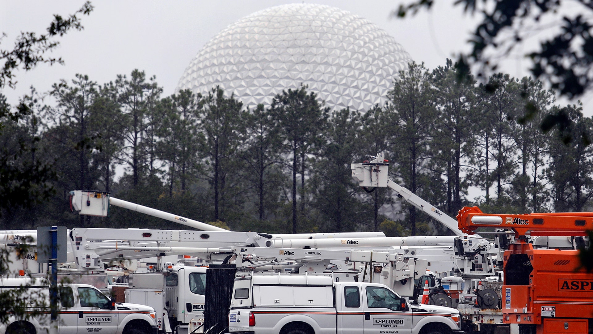 The 'Spaceship Earth' dome looms above a fleet of utility trucks parked in a parking lot at Disney's Epcot theme park