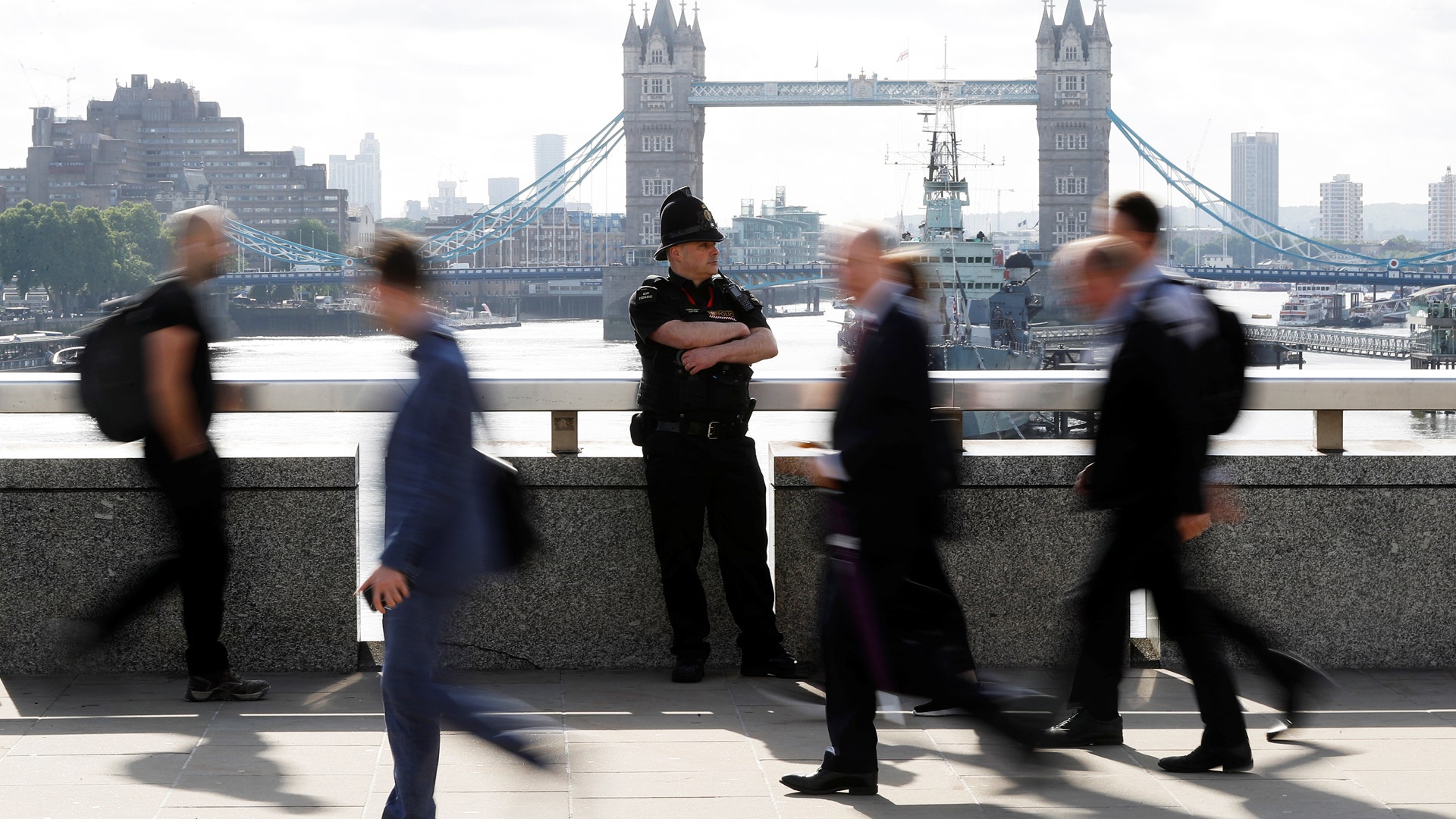 Commuters rush past a City of London police officer standing on London Bridge