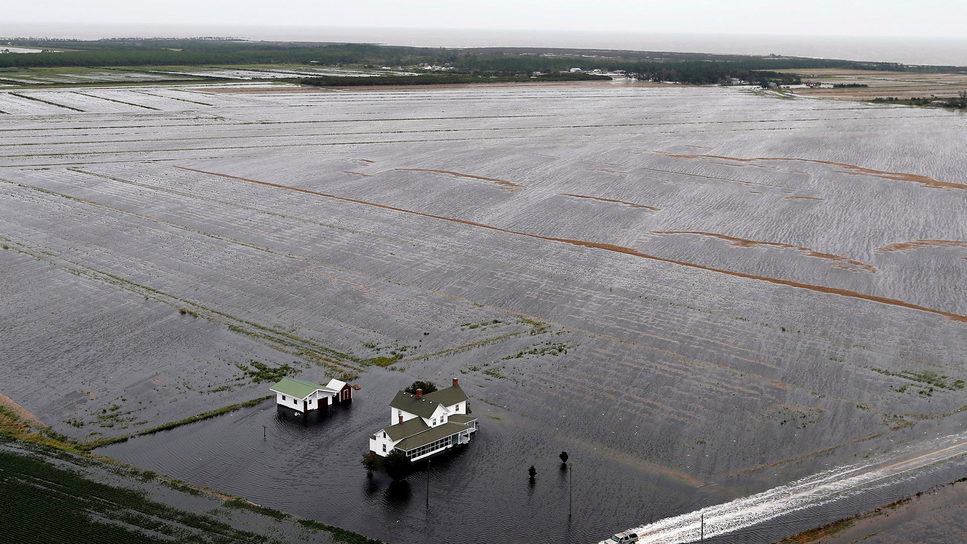 A pickup truck drives on a flooded road past a farm house in Hyde County, North Carolina, Saturday