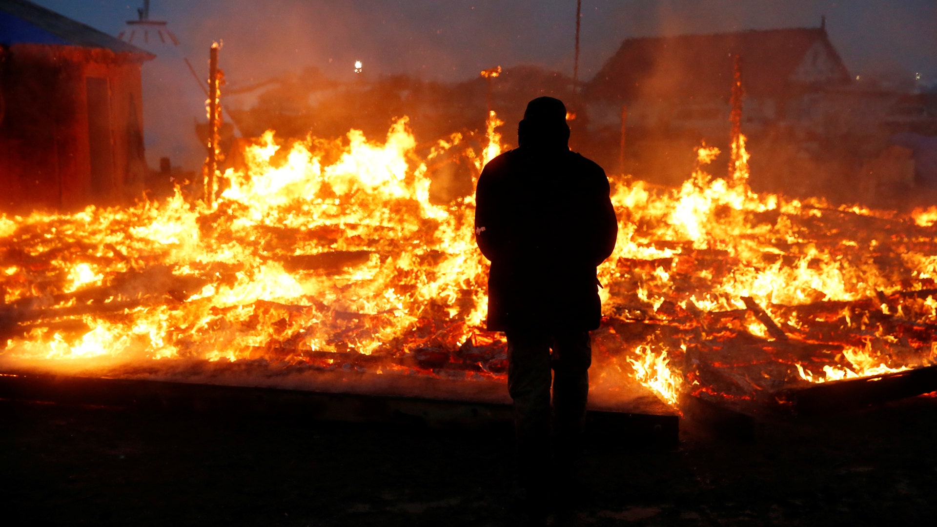 An opponent of the Dakota Access oil pipeline watches a building burn.