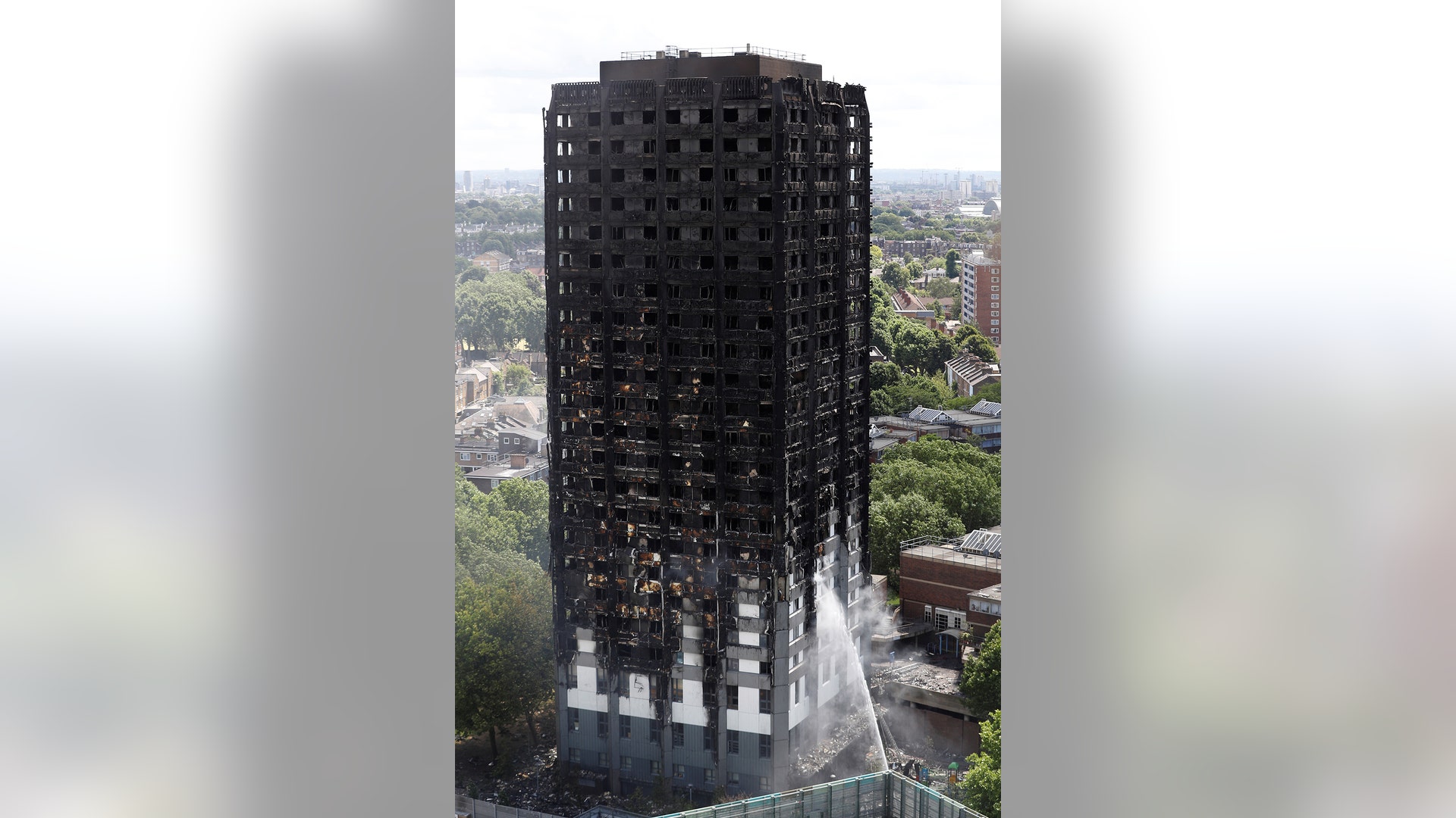 Firemen continue to be spray water onto the apartment building destroyed in a fire in London