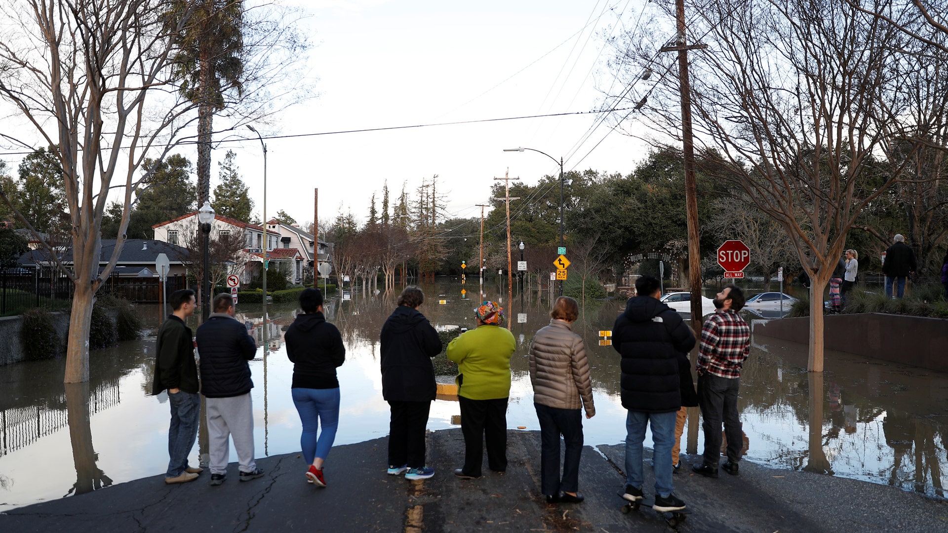 People stand by a flooded street near William Street Park after heavy rains overflowed nearby Coyote Creek in San Jose, California. 