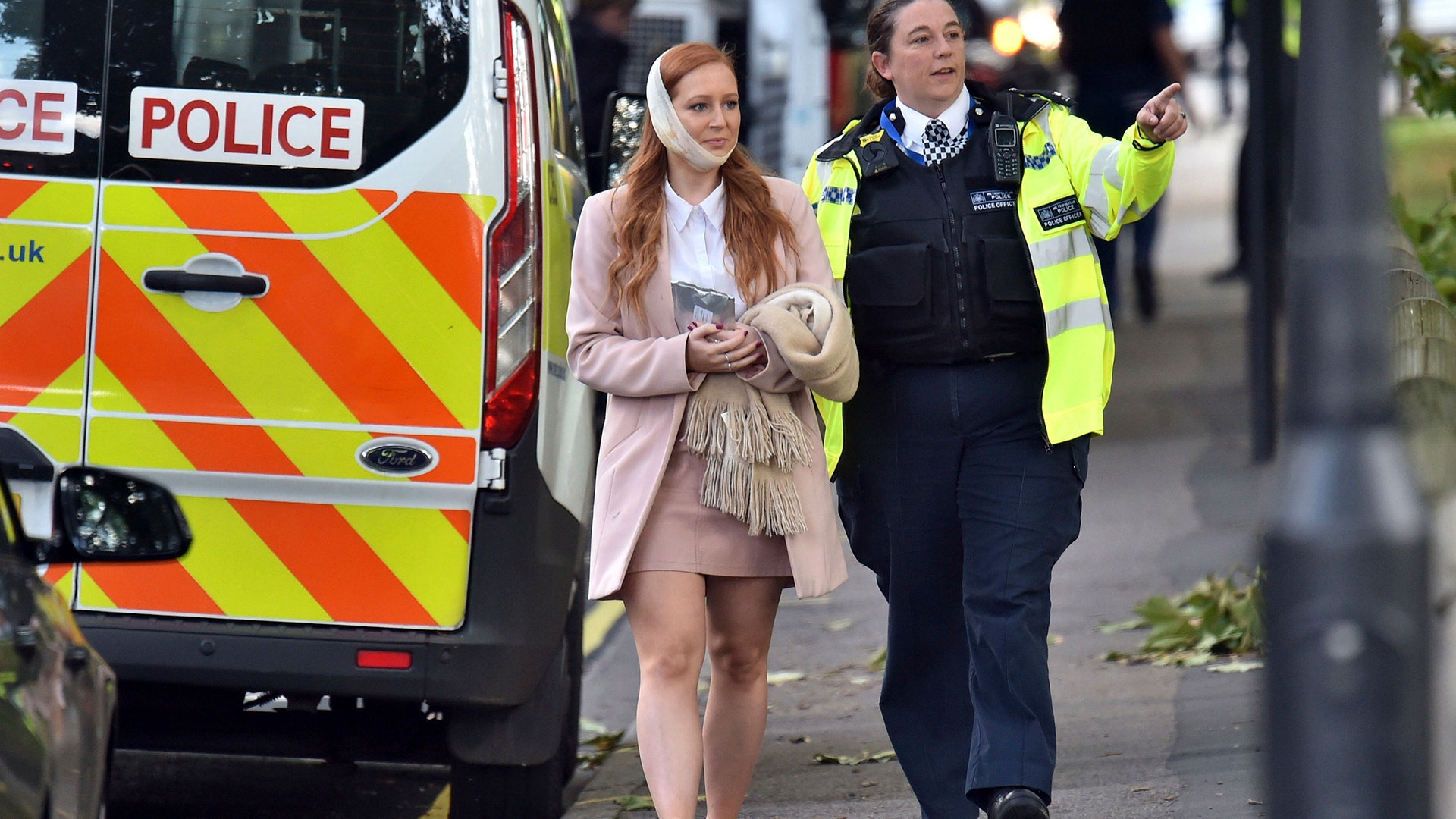 An injured woman is assisted by a police officer in west London after an explosion on a London Underground train