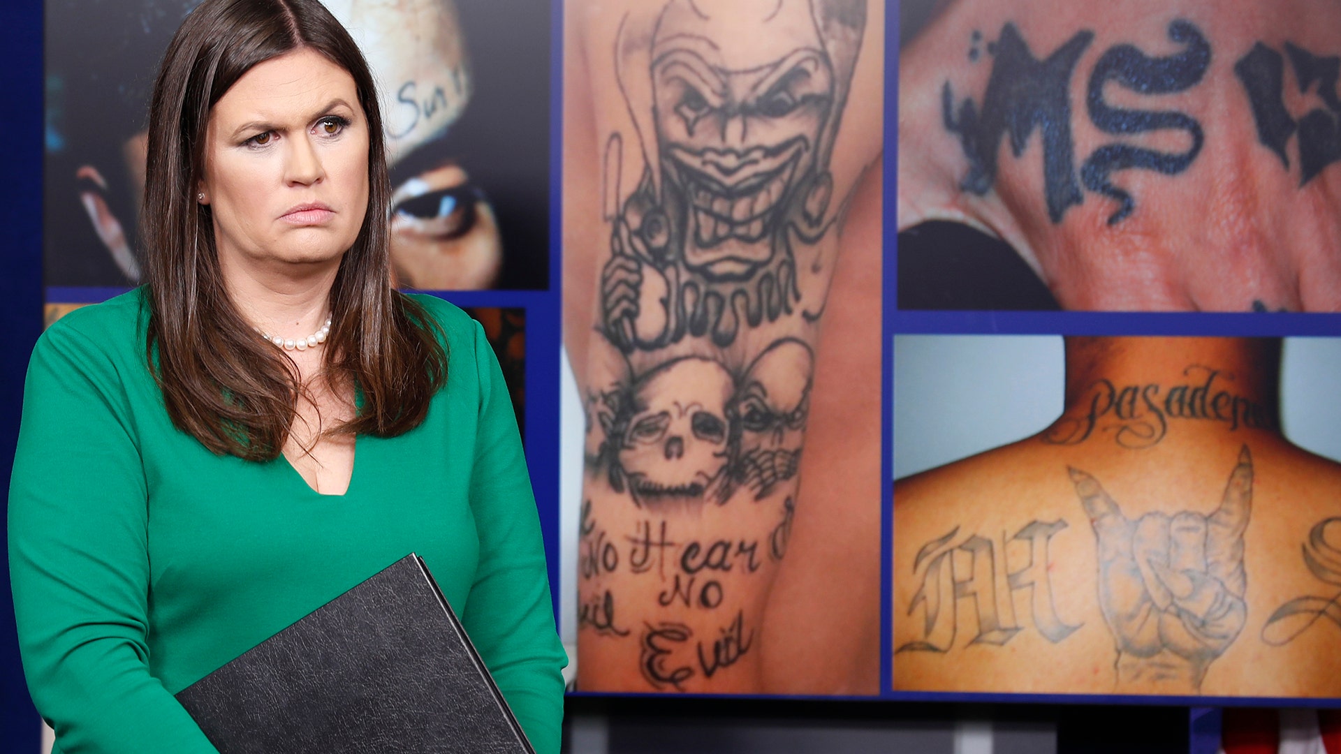 White House press secretary Sarah Huckabee Sanders stands in front of pictures of MS-13 gang tattoos