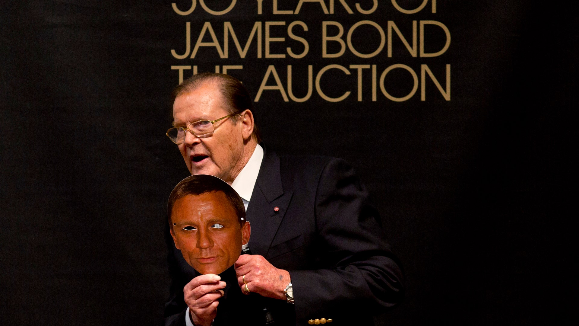 Moore holds a mask of Bond actor Daniel Craig during the 50 Years of James Bond Auction at Christies in London, October 5, 2012