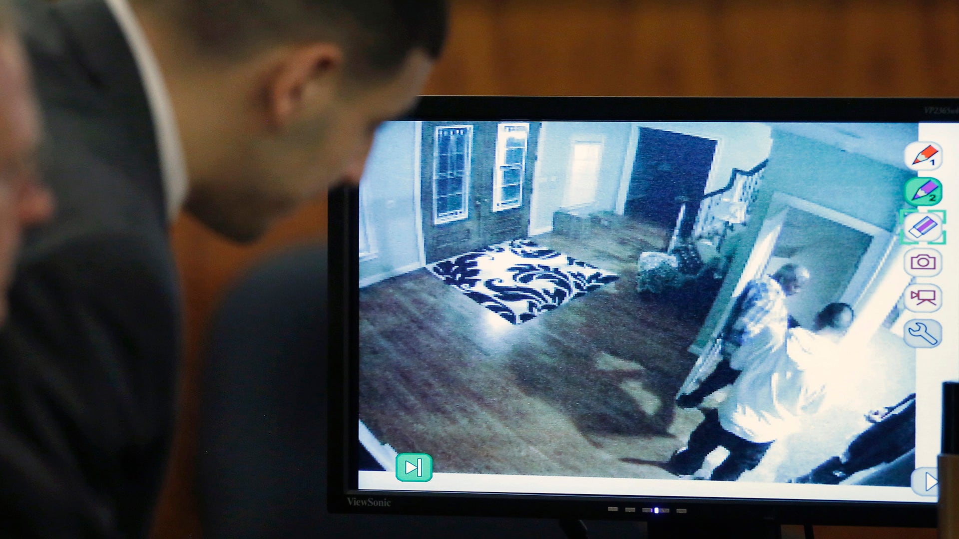 Former New England Patriots player Aaron Hernandez looks on as a still frame from surveillance video is displayed on a monitor during his murder trial.