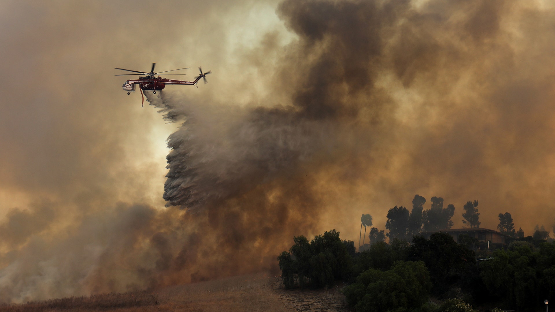 A firefighting helicopter drops water to help save a home during a wind-driven wildfire in Orange, California October 9, 2017