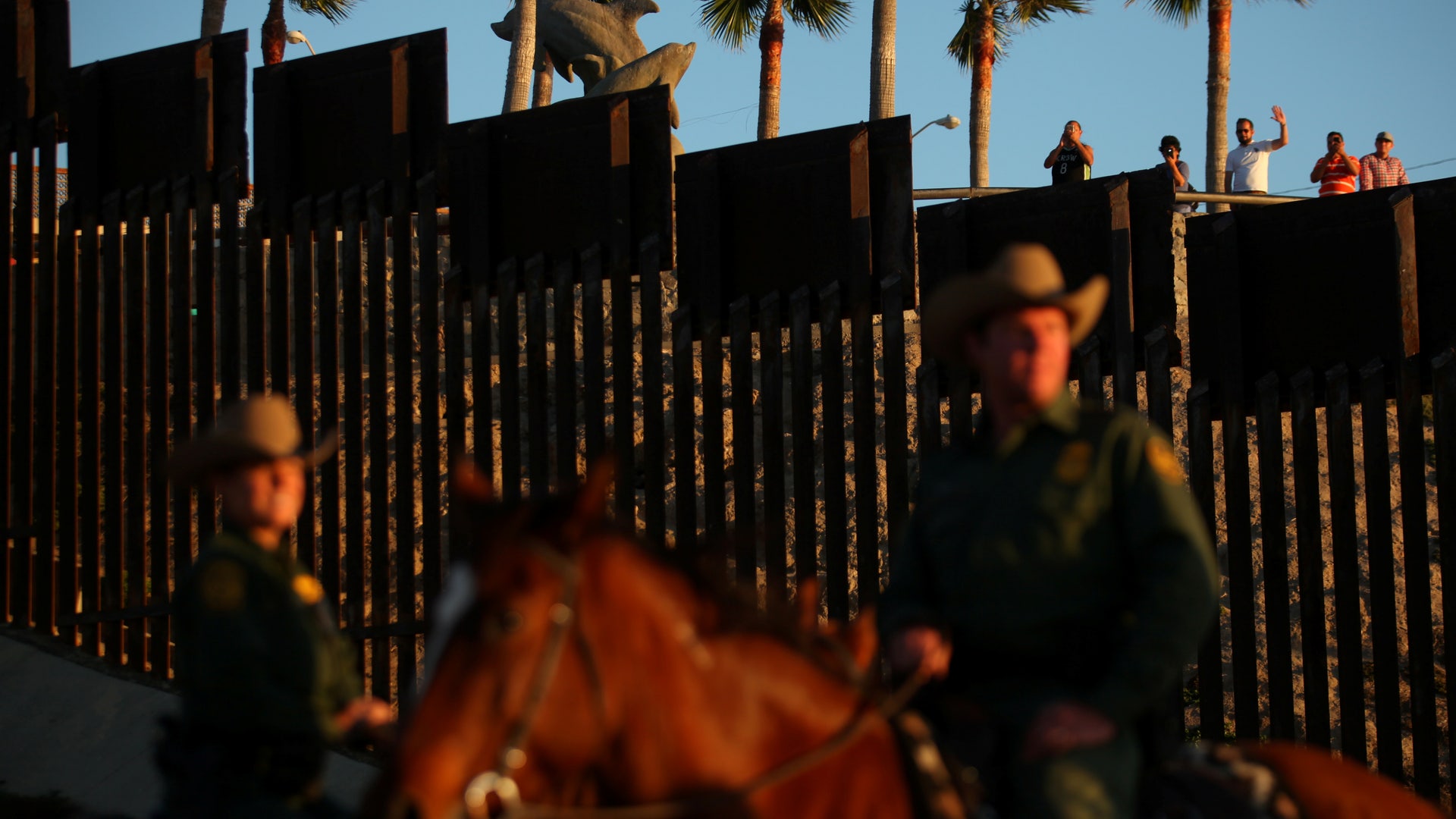 People in Mexico wave at U.S. Border Patrol agents on horseback patrolling the U.S.-Mexico border fence near San Diego, California.