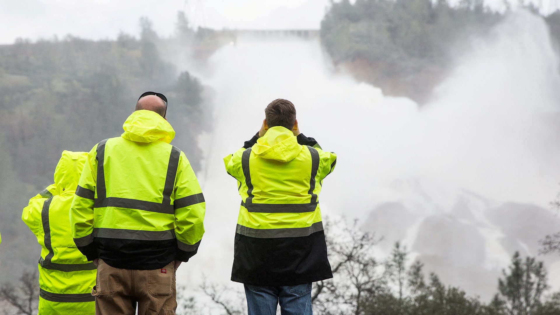 California Department of Water Resources personnel monitor water flowing through a damaged spillway.