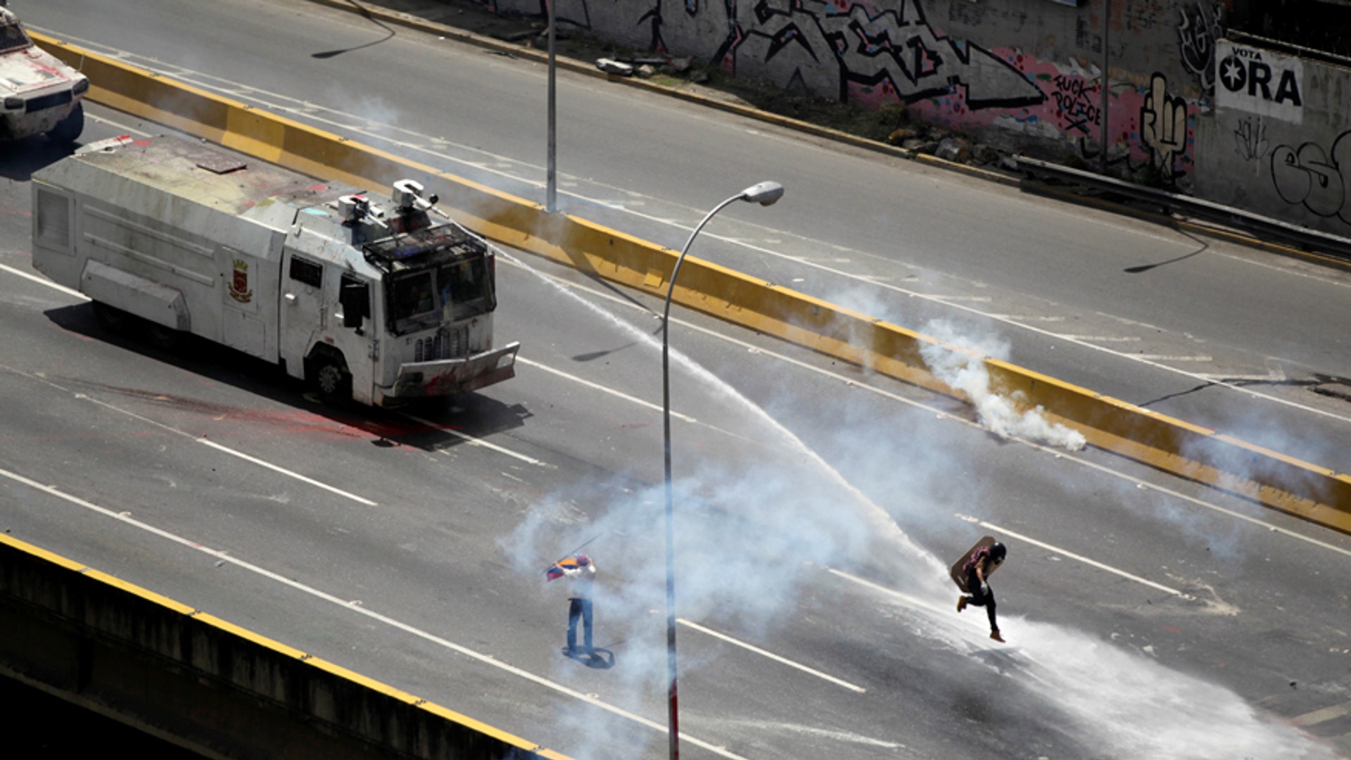 An opposition supporter is hit by a water cannon while clashing with riot security forces during a rally against President Maduro