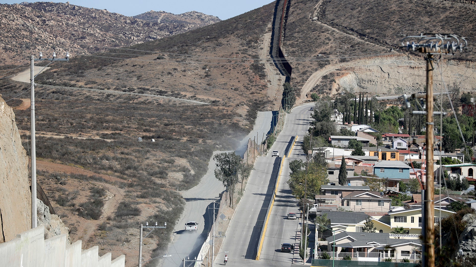 A Border Patrol vehicle drives by the border fence in Tecate, Calif., left, along the metal barrier that lines the border seen from Tecate, Mexico. 