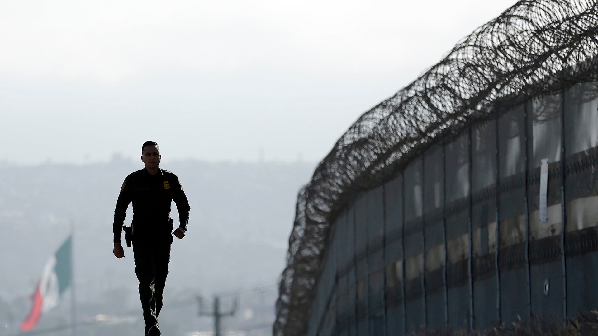 Border Patrol agent Eduardo Olmos walks near the secondary fence separating Tijuana, Mexico, background, and San Diego.