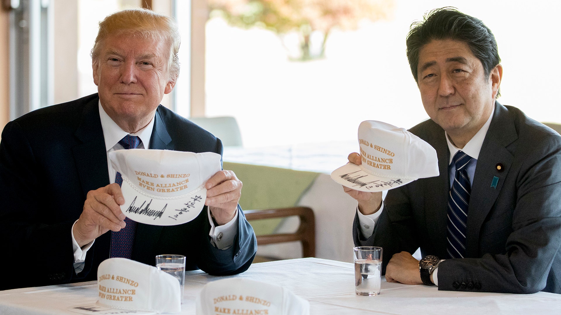 President Trump and Japanese Prime Minister Shinzo Abe display signed hats that say: 