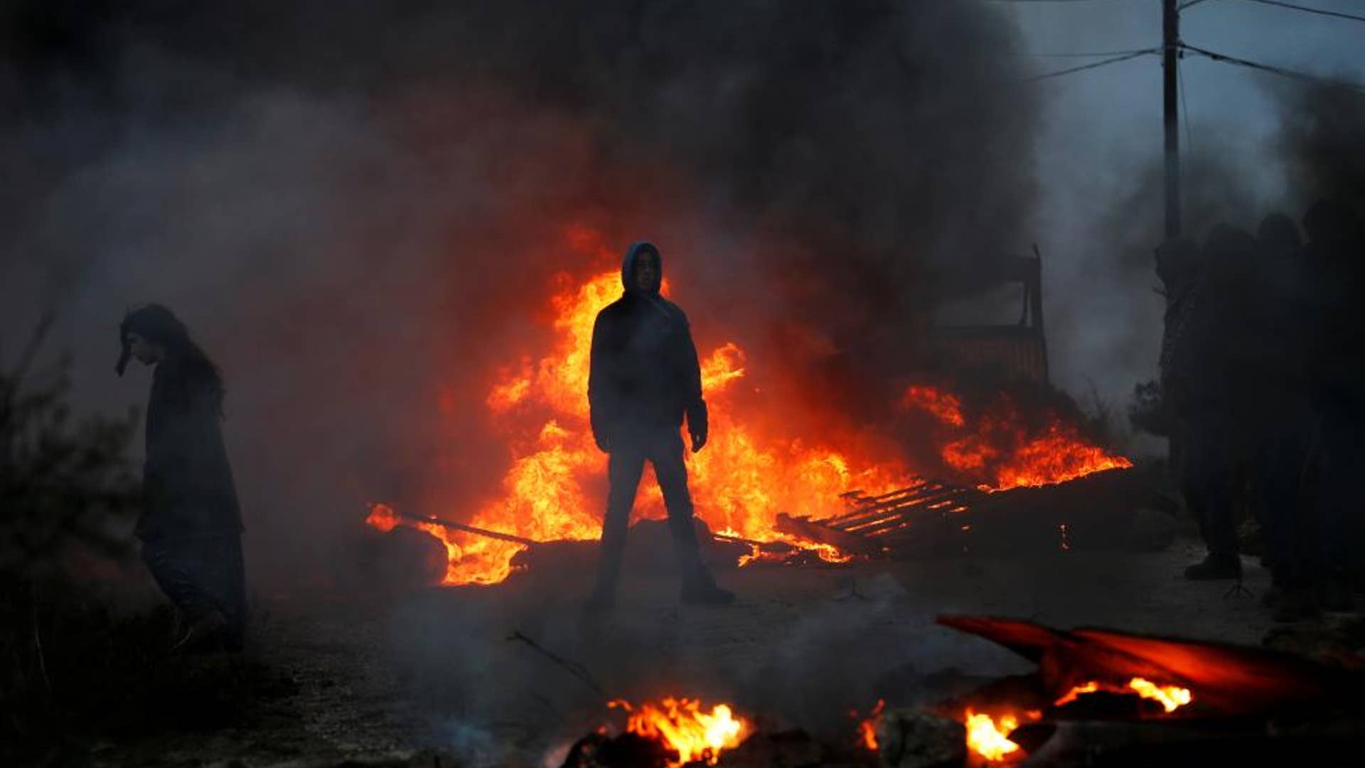 Protesters stand next to fire at the entrance to the Israeli settler outpost of Amona in the occupied West Bank.
