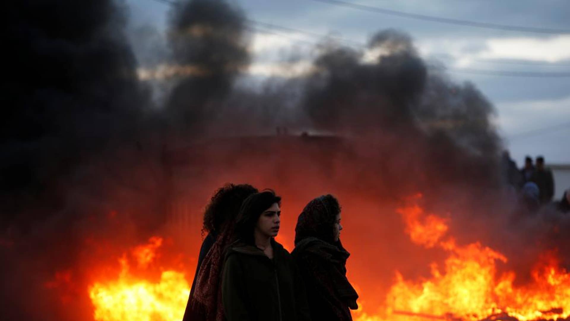 Protesters stand next to fire at the entrance to the Israeli settler outpost of Amona. 