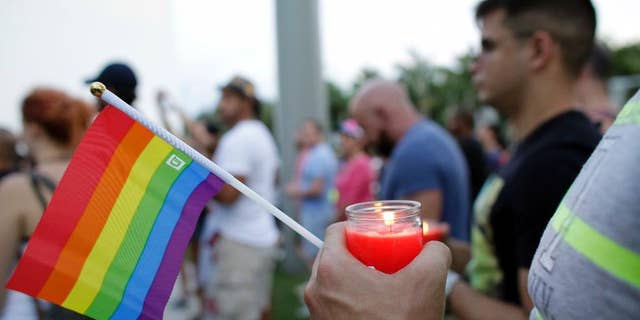 A man holds a candle and a rainbow flag during a vigil in memory of the victims of the Orlando mass shooting, Sunday, June 12, 2016, in Miami Beach, Fla.A gunman opened fire inside a crowded gay nightclub early Sunday, before dying in a gunfight with SWAT officers, police said. (AP Photo/Lynne Sladky)