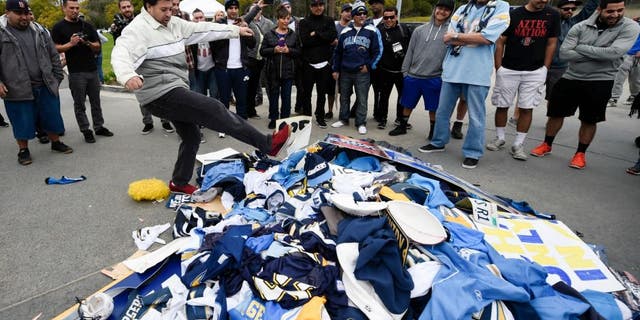 Chris Githens, left, kicks a pile of Chargers memorabilia in front of San Diego Chargers headquarters after the team announced that it will move to Los Angeles Thursday Jan. 12, 2017, in San Diego. (AP Photo/Denis Poroy)