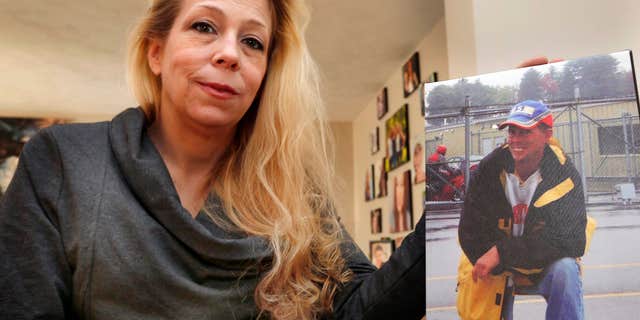 In this photo taken Wednesday, Jan. 13, 2016, Jennifer Cramer Kelley poses at her home with a photo of her brother Christopher Cramer in Nashua, N.H.