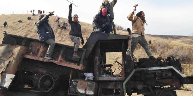FILE - In this Monday, Nov. 21, 2016, file photo, protesters against the Dakota Access oil pipeline stand on a burned-out truck near Cannon Ball, N.D., that they removed from a long-closed bridge a day earlier on a state highway near their camp.