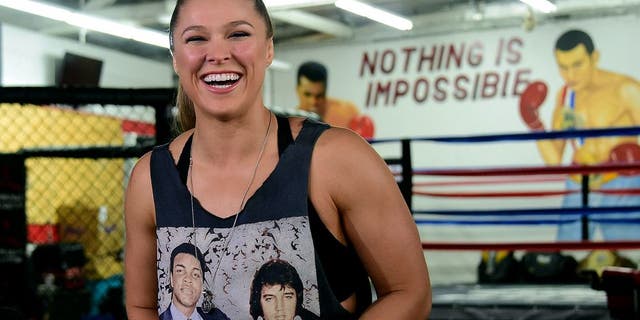 Mixed Martial Arts (MMA) fighter Ronda Rousey, wearing a shirt with portraits of former heavyweight boxing champion Muhammad Ali (L) and the late US singer Elvis Presley (R), responds to questions during media day in Glendale, California on October 27, 2015 ahead of her November 14 fight in Melbourne, Australia against Holly Holm. AFP PHOTO / FREDERIC J. BROWN (Photo credit should read FREDERIC J. BROWN/AFP/Getty Images)