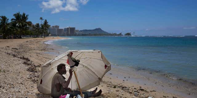FILE - In this Aug. 27, 2015, file photo, a homeless man drinks water while sitting on the beach at Ala Moana Beach Park located near Waikiki in Honolulu.