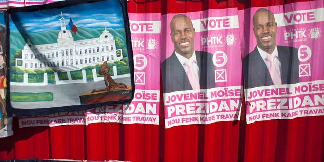FILE - In this Oct. 10, 2015 file photo, campaign posters promoting presidential candidate Jovenel Moise, of the PHTK political party, cover metal sheeting behind a painting for sale of the National Palace in Port-au-Prince, Haiti. The electoral council of Haiti has decided to re-do a presidential election that a special commission determined was marred by fraud. Provisional Electoral Council President Leopold Berlanger said Monday, June 6, 2016, a first round vote will be held Oct. 9. If no one secures a majority, it will be followed by a runoff for the top two contenders on Jan. 8. (AP Photo/Dieu Nalio Chery, File)