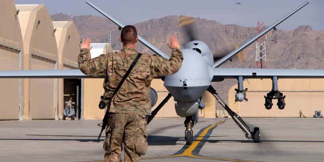 A U.S. airman guides a U.S. Air Force MQ-9 Reaper drone as it taxis to the runway at Kandahar Airfield