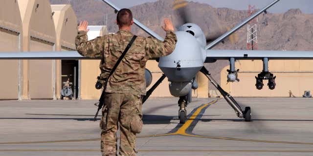 A U.S. airman guides a U.S. Air Force MQ-9 Reaper drone as it taxis to the runway at Kandahar Airfield