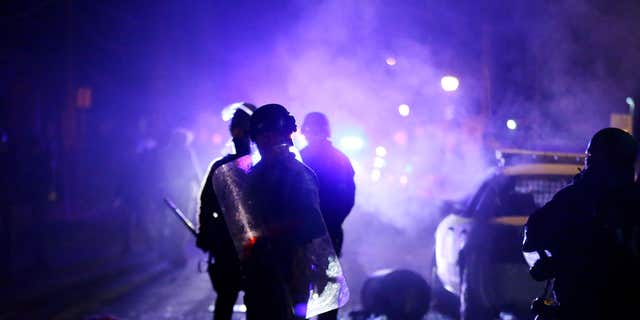 FILE - In this Nov. 25, 2014 file photo, police officers watch protesters as smoke fills the streets in Ferguson, Mo.