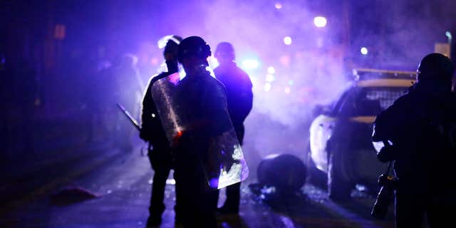 FILE - In this Nov. 25, 2014 file photo, police officers watch protesters as smoke fills the streets in Ferguson, Mo.