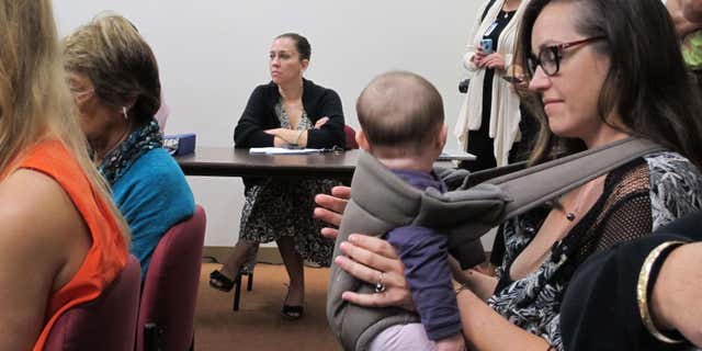 Colleen Chapman, an Oahu resident who's concerned about her children's exposure to pesticide, listens to testimony while holding her daughter at a legislative hearing on Tuesday, Feb. 9, 2016 in Honolulu.