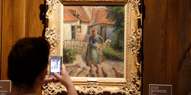 FILE - In this Feb. 8, 2014, file photo, a visitor to the Fred Jones Jr. Museum of Art at the University of Oklahoma in Norman, Okla., takes a photograph of a piece called “Shepherdess Bringing in Sheep” by French impressionist artist Camille Pissarro, at the museum.