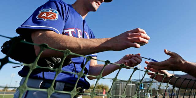 FILE - In this Feb. 21, 2016, file photo, Texas Rangers pitcher Cole Hamels signs autographs during spring training baseball practice, in Surprise, Ariz.