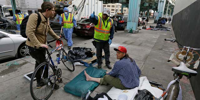 A city worker tells a homeless man that the area next to him on is about to be power washed and points to an area he might want to move Friday, Feb. 26, 2016, in San Francisco.
