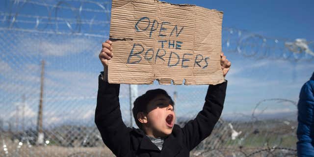 Feb. 27, 2016: A boy shouts slogans as he holds a placard during a protest by refugees and migrants in front of the wire fence that separates the Greek side from the Macedonian one at the northern Greek border station of Idomeni.