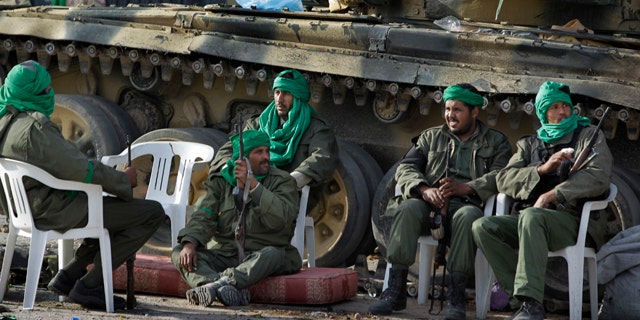 March 11: In this photo taken during a government organized visit for foreign media, pro-Qaddafi soldiers sit by their tank next to a destroyed building in the main square of Zawiya.