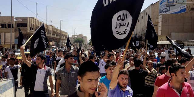 FILE - In this June 16, 2014 file photo, demonstrators chant pro-Islamic State group slogans as they carry the group's flags in front of the provincial government headquarters in Mosul, Iraq.