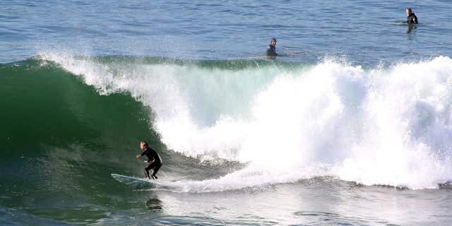 FILE - In this Tuesday, Dec. 8, 2015, file photo, surfers ride a wave at Lunada Bay in Palos Verdes Estates, Calif.
