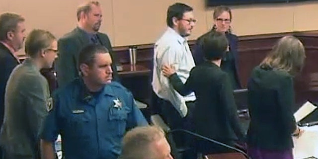 James Holmes, top fourth from right in light-colored shirt, gets a pat on the arm from a member of his defense team following testimony from Holmes' younger sister Chris.