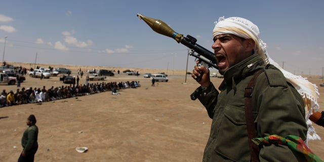April 8: A Libyan rebel fighter, holding a rocket launcher, shouts religious slogans after gun shots were heard as fellow comrades offer prayers in the background in Ajdabia, Libya.