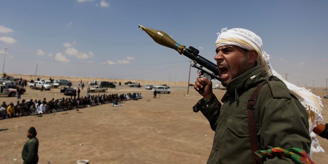 April 8: A Libyan rebel fighter, holding a rocket launcher, shouts religious slogans after gun shots were heard as fellow comrades offer prayers in the background in Ajdabia, Libya.