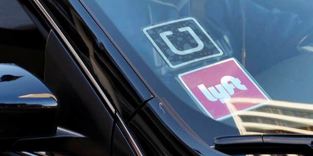 FILE - In this Jan. 12, 2016, file photo, a driver displaying Lyft and Uber stickers on his front windshield drops off a customer in downtown Los Angeles.
