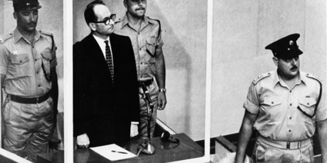 1962: Adolf Eichmann stands in his glass cage, flanked by guards, in the Jerusalem courtroom where he was tried for war crimes committed during World War II. The basics of Adolf Eichmann's story are well-documented. He was commonly known as the "architect of the Holocaust" for his role in coordinating the Nazis' policy of genocide. He fled Germany only to be captured in Argentina by the Mossad, taken to Israel for trial, and hanged.
