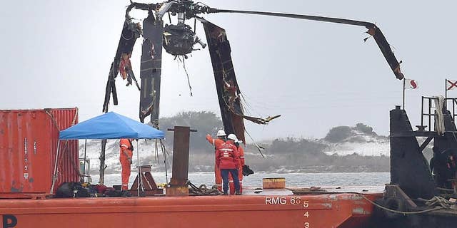 Crews lower a piece of a Black Hawk helicopter onto a barge in the Santa Rosa Sound near Pritchard Point, Friday, March 13, 2015, in Navarre, Fla. The helicopter, which crashed in dense fog during a training mission, was carrying seven Marines based in North Carolina along with four National Guard soldiers from Louisiana. All were killed. (AP Photo/Northwest Florida Daily News, Nick Tomecek)
