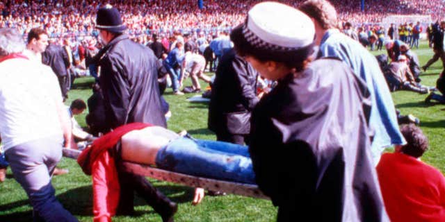 FILE - In this April 15, 1989 file photo police, stewards and supporters tend and care for wounded supporters on the field at Hillsborough Stadium, in Sheffield, England.
