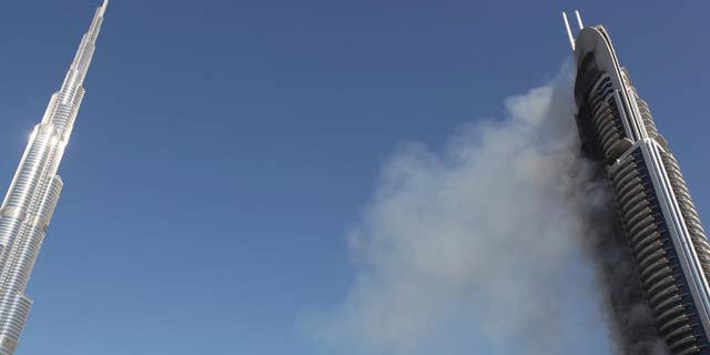 FILE - In this Jan. 1, 2016 file photo, smoke billows from the 63-story The Address Downtown skyscraper near the Burj Khalifa, the world's tallest building, in Dubai, United Arab Emirates. The developer of the world's tallest building says it will collect $332.4 million from its insurer to cover damage sustained during a dramatic New Year's Eve fire at one of its Dubai hotels. Emaar Properties said in a filing to the Dubai Financial Market that it has agreed with Orient Insurance to recover the 1.22 billion dirham claim related to the Dec. 31, 2015 blaze. (AP Photo/Jon Gambrell, File)