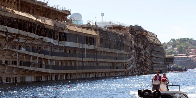 FILE - In this Sept. 18, 2013 file photo, a small boat navigates past the damaged side of the Costa Concordia ship after it was pulled upright, on the Tuscan Island of Giglio, Italy. Divers searching the submerged part of the wreck of the cruise ship have found the remains of one of the two people still missing from the 2012 disaster. Officials believe the remains belong to Russel Rebello, an Indian waiter. Thirty-two people died when the Concordia slammed into a reef off the Tuscan island of Giglio and capsized on Jan. 13, 2012. (AP Photo/Andrew Medichini, file)