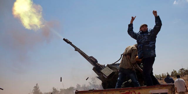 May 7: A rebel fighter gestures as an anti-aircraft gun fires into the sky in a gesture to salute the dead, during the funeral of three rebel fighters killed by Muammar al-Qaddafi forces, Benghazi, Libya.